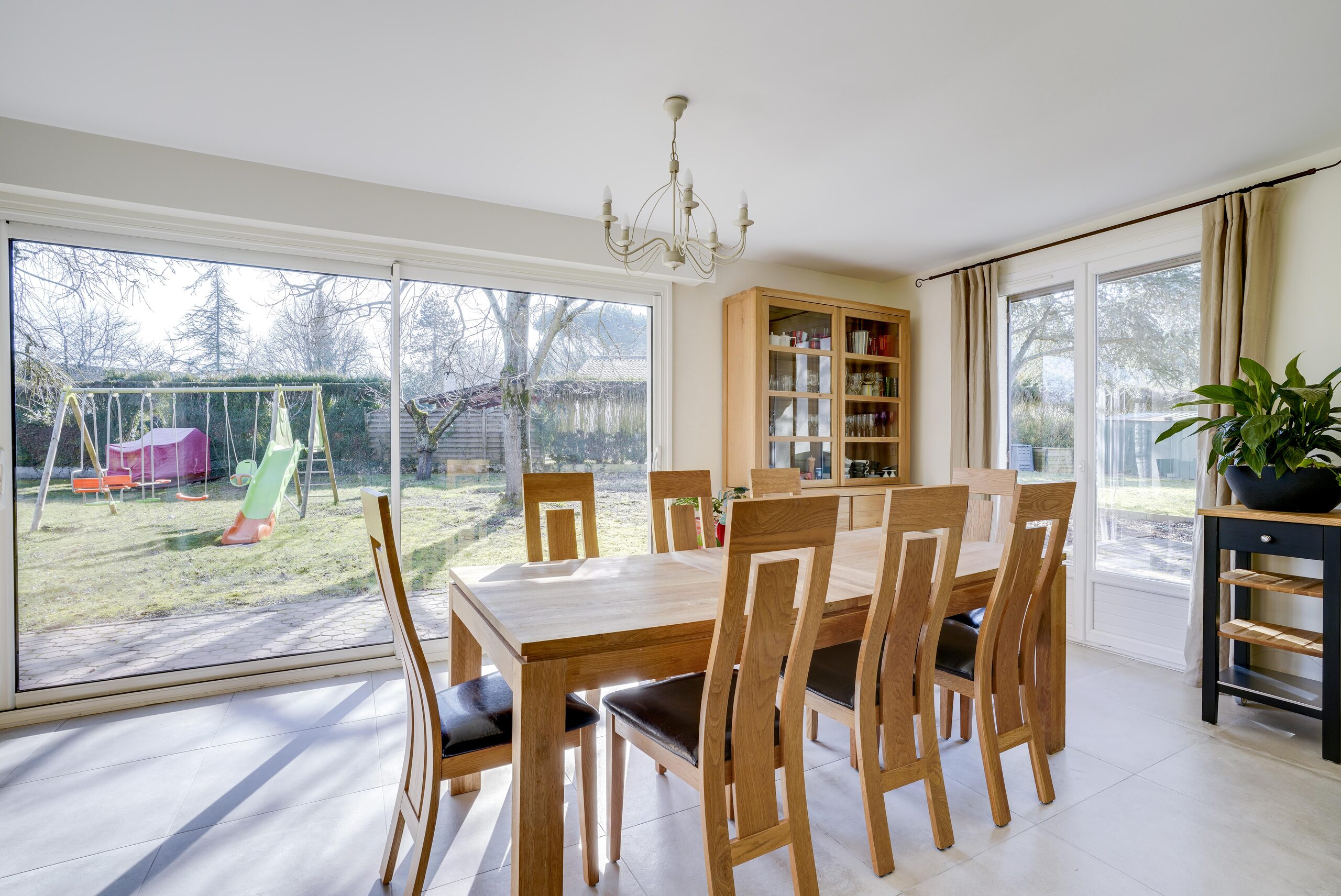 Salle à manger de maison rénovée avec table en bois et baie vitrée sur jardin