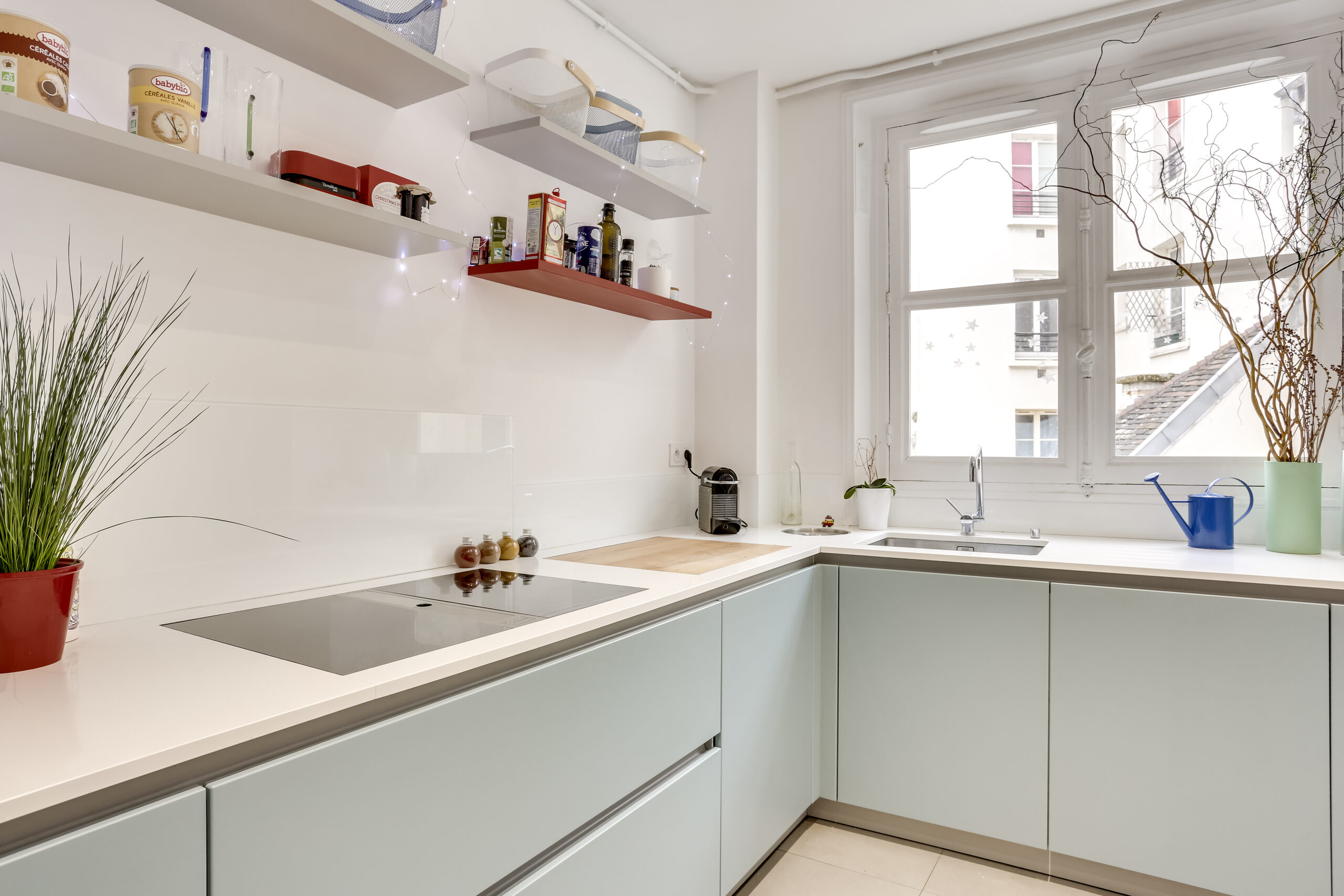 Cuisine compacte minimaliste avec armoires bleu clair et plans blancs, adaptée à un appartement