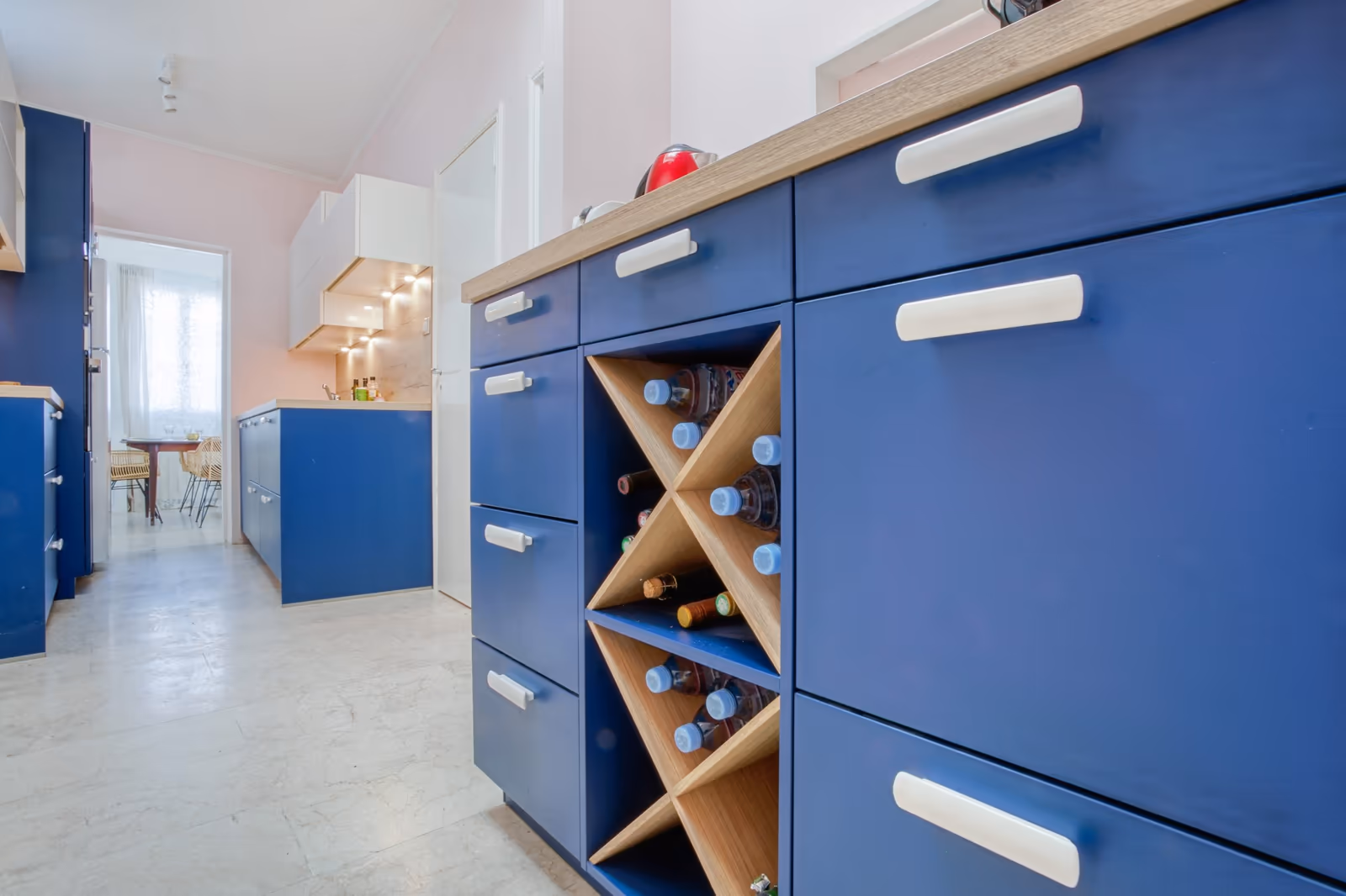 Détail des rangements bleus avec casier à bouteilles en bois et poignées blanches