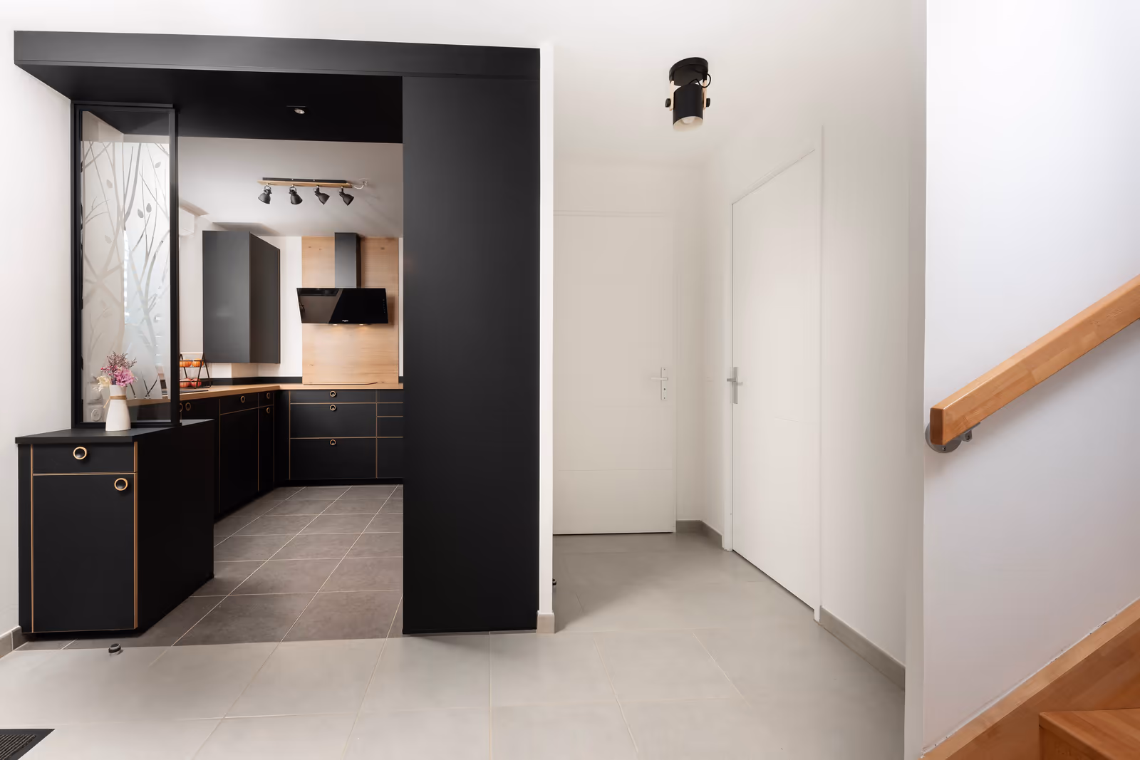 Vue depuis l'entrée sur la cuisine noire avec hotte et plan de travail en bois